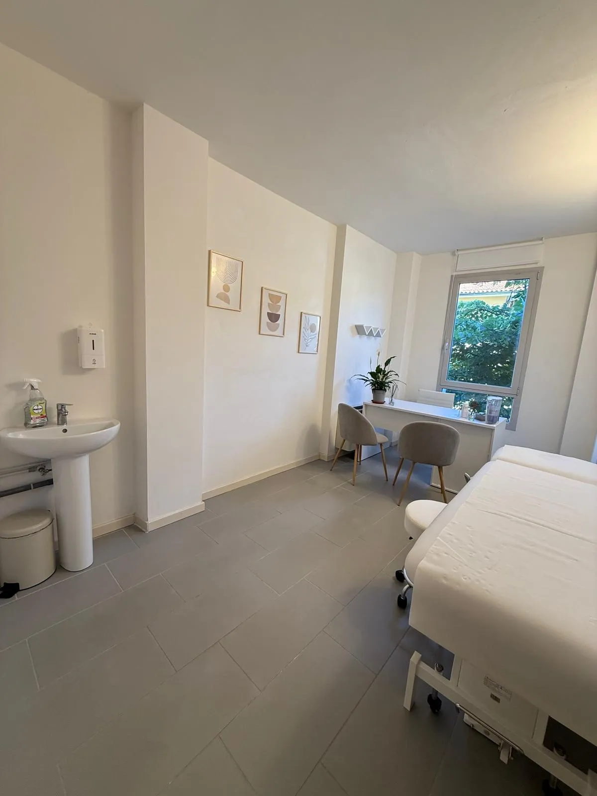 Studio di consulenza con lavabo, trittico grafico e finestra sul fogliame