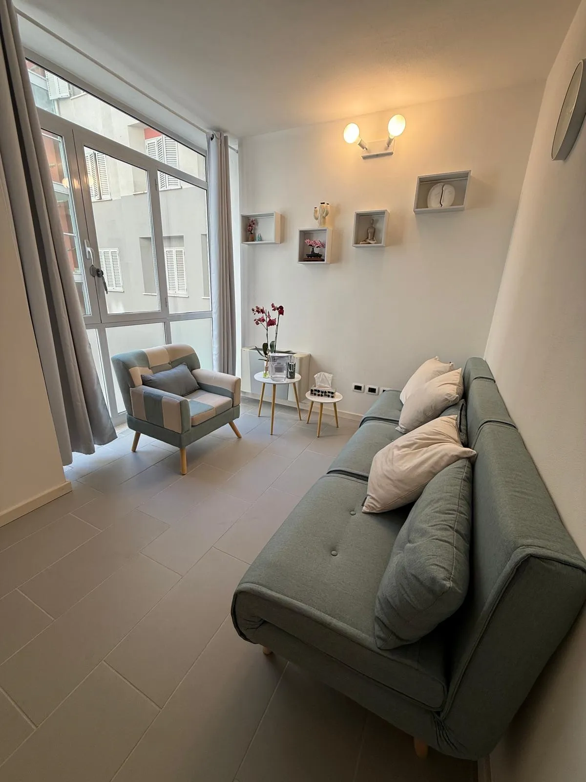 Sala di consulenza con vetrata, divano salvia e poltrona a cuscini